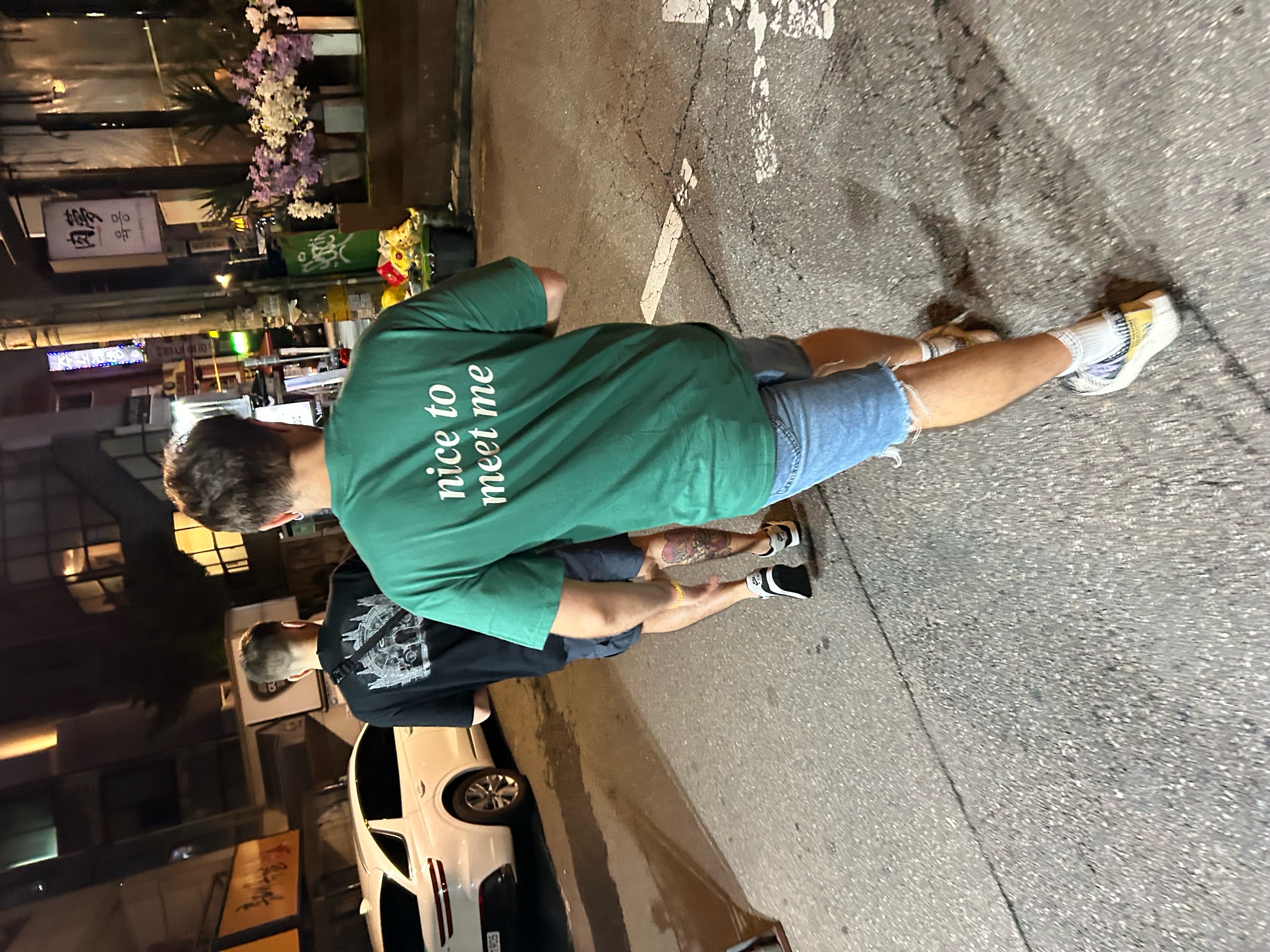 Person wearing the green nice to meet me SORRY BABY shirt on a Sheung Wan street at night