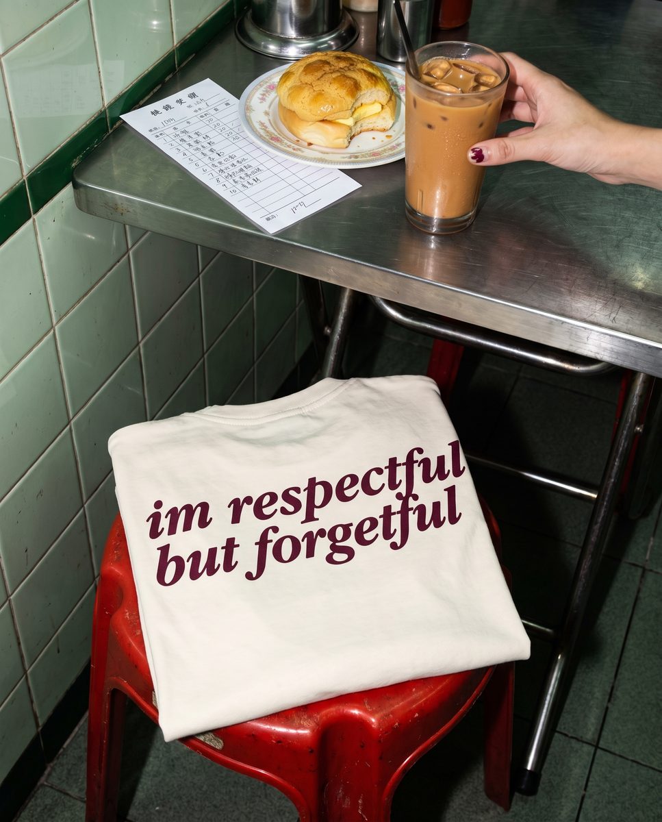 Cream SORRY BABY shirt reading im respectful but forgetful, folded over a red stool in a cha chaan teng