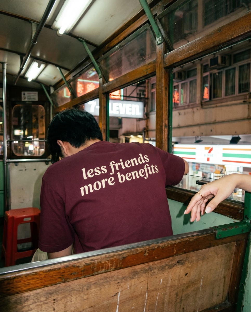 Burgundy SORRY BABY shirt reading less friends more benefits on the upper deck of a Hong Kong tram