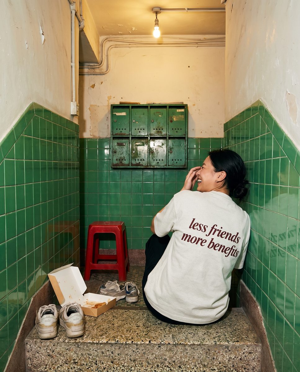Oat grey SORRY BABY shirt reading less friends more benefits, worn in a Hong Kong night scene