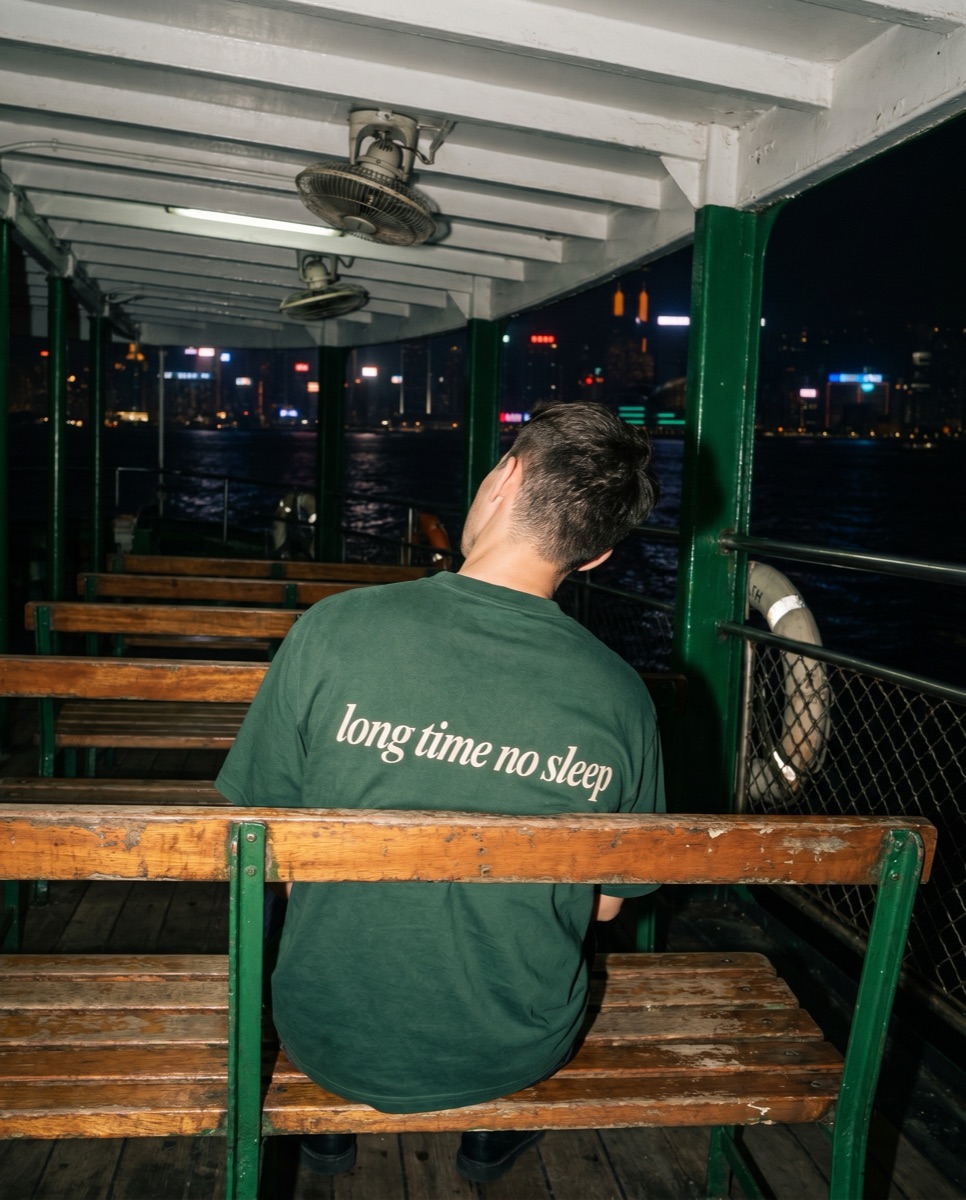 Forest green SORRY BABY shirt reading long time no sleep on a wooden bench of the Star Ferry at night